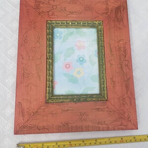 May include: A red wooden picture frame with a carved floral design. The frame has a gold inner border and a light blue background with a floral pattern.