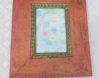 May include: A red wooden picture frame with a carved floral design. The frame has a gold inner border and a light blue background with a floral pattern.