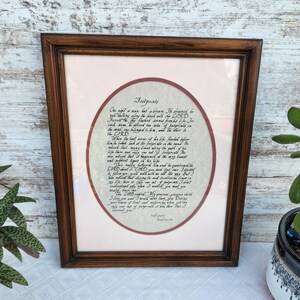 May include: A framed print with the poem "Footprints" in a brown wooden frame. The poem is written in black ink on a cream-colored background, surrounded by a maroon border. The text is centered within the frame.
