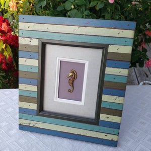 May include: A framed picture featuring a gold seahorse on a purple background. The frame is made of wood with a distressed blue, green and white paint finish.