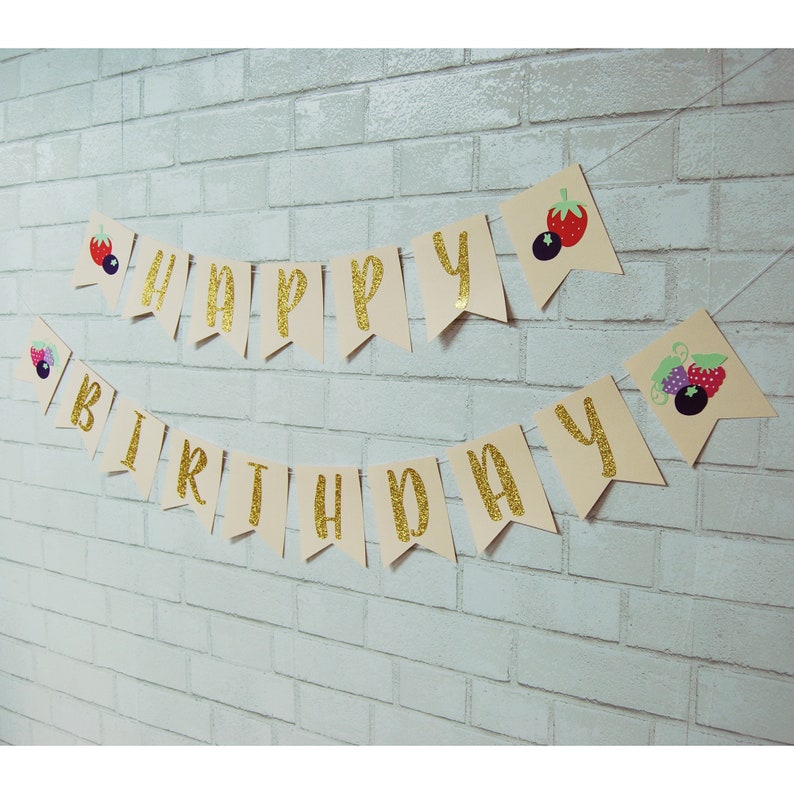May include: A beige banner with gold glitter letters spelling "Happy Birthday" with berry and strawberry illustrations on each end.