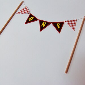 May include: A red and white checkered banner with the word "ONE" in yellow letters. The banner is strung on two wooden dowels.