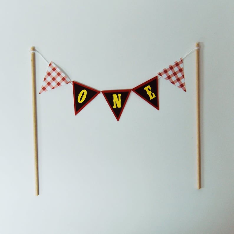 May include: Red and white gingham cake topper with the word "ONE" in yellow letters.