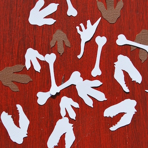 Peut inclure: Des découpes en papier blanc d'os et d'empreintes de dinosaures sur un fond de bois rouge. Il y a aussi des découpes en papier brun d'empreintes de dinosaures.
