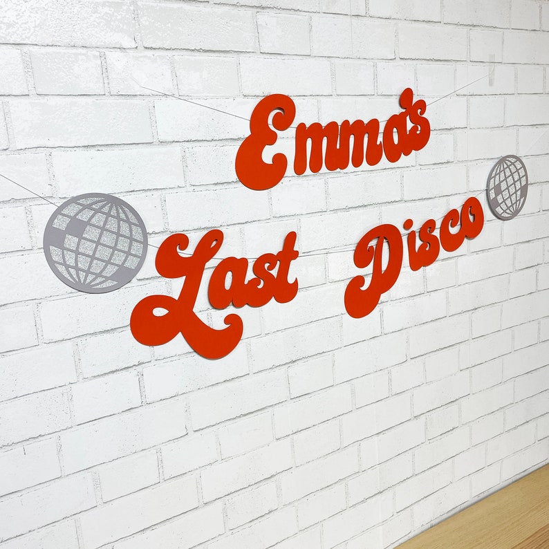 May include: Orange and silver party banner with the text "Emma's Last Disco" and two silver disco ball shapes.
