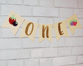 May include: A yellow banner with the word "ONE" in gold glitter letters. The banner has berry-themed decorations on each end.