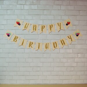 May include: A beige banner with gold glitter letters spelling "Happy Birthday" with berry and strawberry illustrations on each end.