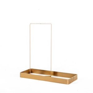 May include: A gold metal rectangular shelf with a single vertical bar across the top.
