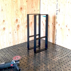 May include: Two black metal table legs with a welded crossbar. The legs are sitting on a metal surface with a grid pattern.