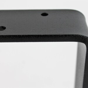 Peut inclure: &Eacute;querre d'&eacute;tag&egrave;re en m&eacute;tal noir de forme carr&eacute;e avec des bords arrondis. L'&eacute;querre comporte trois trous pour le montage.