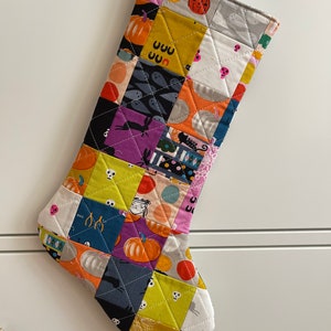 May include: A patchwork Halloween stocking with a variety of colorful fabrics featuring pumpkins, ghosts, skulls, and other Halloween motifs.