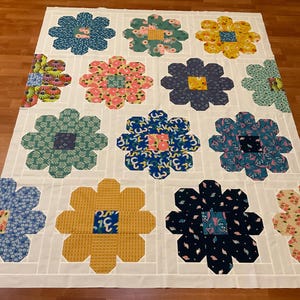 May include: A handmade quilt featuring large, colorful flower patterns on a white background. The flowers are in shades of blue, pink, yellow, and green, with patterned centers. The quilt is made of fabric squares and rectangles.