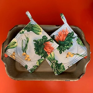 May include: Two blue and white pot holders with a floral and vegetable print. The pot holders are on a gray metal tray.