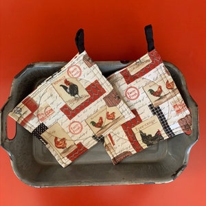Könnte beinhalten: Zwei rote und weiße gequiltete Topflappen mit einem Bauernhof-Thema. Die Topflappen zeigen ein Huhn, einen Hahn und den Text "Farm Fresh".