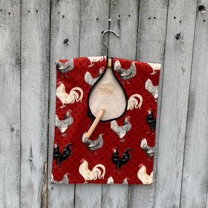 May include: Red fabric garment bag with a black trim and a white rooster pattern. The bag has a hanger loop and a label that reads "Daughter of the Charm".