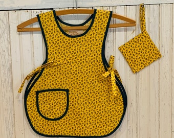 May include: A yellow and green apron with a small pocket and a matching fabric pouch. The apron has a green trim and a small label that reads "Enchanter of the Charm".