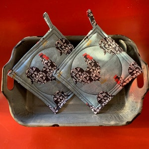 Könnte beinhalten: Zwei blaue und weiße Topflappen mit einem Hahn-Design. Die Topflappen befinden sich in einer Metallschale auf einer roten Oberfläche.