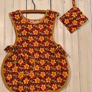 May include: A red and yellow floral print apron with a matching pot holder. The apron has a large pocket and ties at the waist.