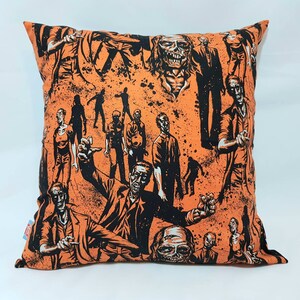 May include: Orange cushion with a black and white print of zombies. The cushion features a variety of zombie characters in different poses.