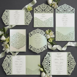 May include: A collection of elegant wedding invitations in various designs. The invitations feature intricate laser-cut patterns in a soft green hue, with white inserts displaying event details. Floral accents and ribbons complement the stationery.
