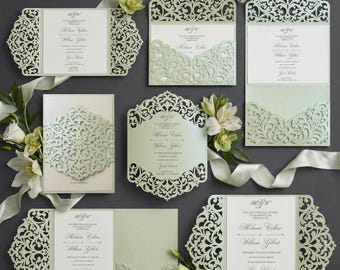 May include: A collection of elegant wedding invitations in various designs. The invitations feature intricate laser-cut patterns in a soft green hue, with white inserts displaying event details. Floral accents and ribbons complement the stationery.