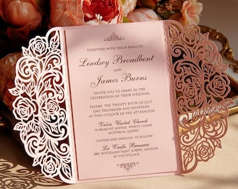 Può includere: Un invito di nozze rosa con intricati disegni floreali tagliati al laser. L'invito include i nomi "Lindsey Broadbent" e "James Burns", insieme ai dettagli del matrimonio. L'invito è presentato davanti a dei fiori.
