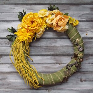 May include: A green fabric wreath decorated with yellow and orange silk flowers and antique keys.