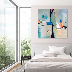 May include: Abstract painting with geometric shapes in shades of blue, green, pink, and orange. The painting is hanging on a white wall above a bed with white bedding.