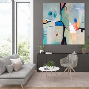 May include: Abstract painting with a mix of blue, green, pink, and orange colors. The painting is framed and hanging on a gray wall in a living room setting.