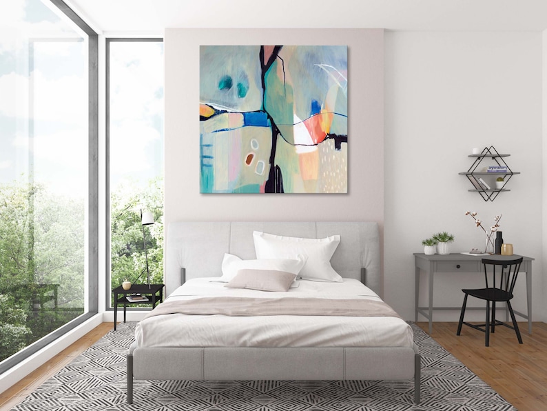 May include: Abstract painting with geometric shapes in shades of blue, green, pink, and orange. The painting is hanging on a white wall above a bed with white bedding.