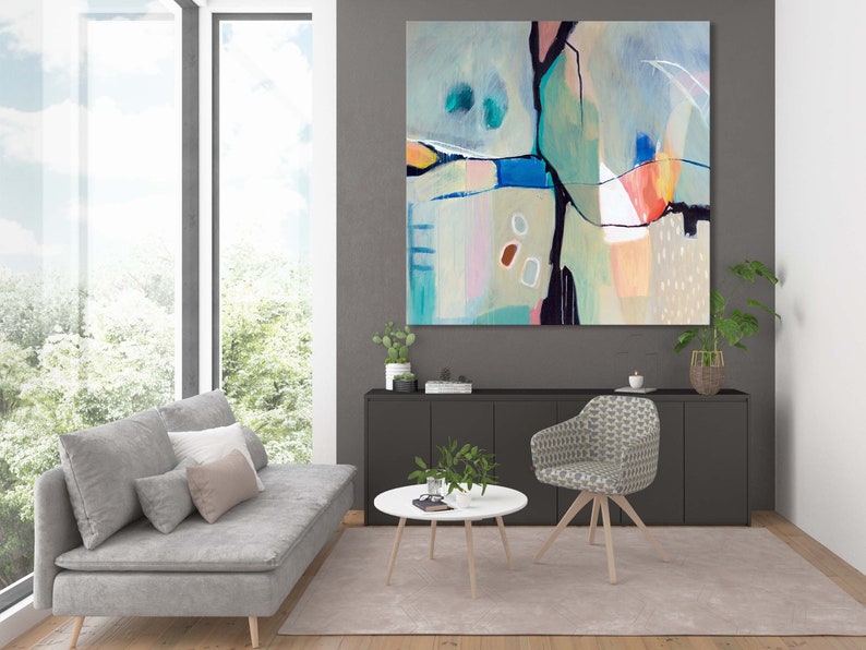 May include: Abstract painting with a mix of blue, green, pink, and orange colors. The painting is framed and hanging on a gray wall in a living room setting.