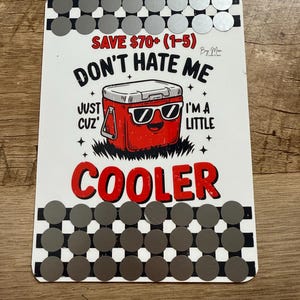 Puede incluir: Un letrero rectangular blanco con un gráfico de nevera roja con gafas de sol y el texto "DON'T HATE ME JUST CUZ I'M A LITTLE COOLER". El letrero tiene un borde a cuadros blanco y negro y acentos de círculo plateado.