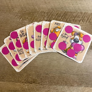 May include: A collection of greeting cards with cartoon dog illustrations and pink accents. Each card features a different dog design and a phrase like "Be Mine" or "So Loved". The cards have a pink circle on each card.