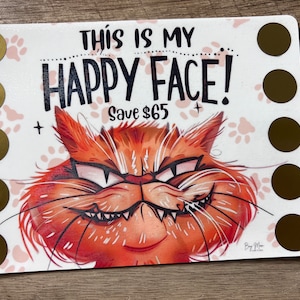 May include: A white card with a cartoon orange cat with a mischievous grin. The card says "This is my Happy Face! Save $65". There are gold circles on the left and right sides of the card.