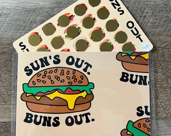 Puede incluir: Un protector de página de plástico transparente con una tarjeta marrón y blanca en su interior. La tarjeta tiene una hamburguesa de dibujos animados amarilla, marrón y verde con el texto "Sun's Out, Buns Out". La tarjeta también tiene una hamburguesa de dibujos animados más pequeña en la esquina inferior derecha. La parte superior del protector de página tiene una tarjeta blanca con una cuadrícula de 16 círculos dorados con el texto "Buns Out" en el lado derecho.