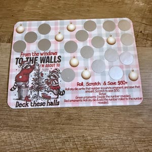 Puede incluir: Tarjeta de rascar con temática navideña con un fondo a cuadros rosa y blanco. La tarjeta presenta ilustraciones de mapaches decorando un árbol de Navidad y el texto "From the windows to the walls, I'm about to Deck these halls." Contiene círculos para rascar e instrucciones.
