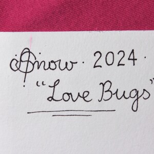 May include: A white card with black ink handwriting that says "Snow 2024" and "Love Bugs" with a double line underneath.