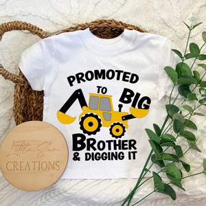 May include: White t-shirt with a yellow construction vehicle graphic and the text "Promoted to Big Brother & Digging It".