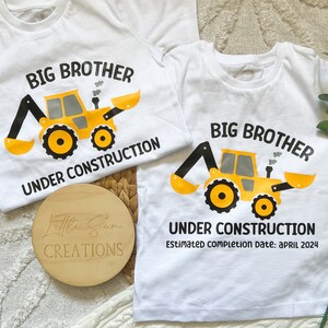 May include: Two white t-shirts with a yellow construction vehicle graphic and the text "Big Brother Under Construction". The smaller shirt has the text "Estimated completion date: April 2024".