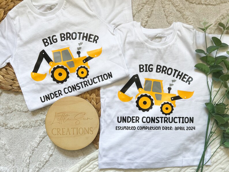 May include: Two white t-shirts with a yellow construction vehicle graphic and the text "Big Brother Under Construction". The smaller shirt has the text "Estimated completion date: April 2024".