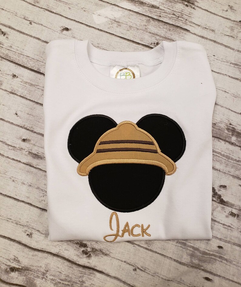 May include: White t-shirt with an embroidered image of Mickey Mouse wearing a safari hat. The name "Jack" is embroidered below the image.