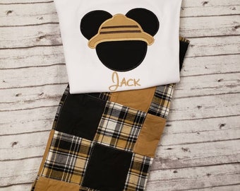 May include: White t-shirt with a black and brown embroidered Mickey Mouse wearing a safari hat. The shirt has the name "Jack" embroidered below the image. The shirt is paired with brown, black, and white plaid shorts.