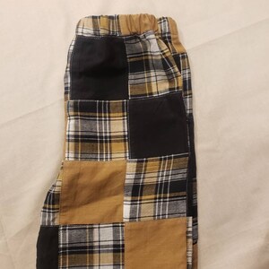 May include: Patchwork shorts with a black and yellow plaid pattern. The shorts have an elastic waistband and are made of a soft, comfortable fabric.