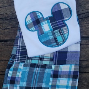 May include: A white t-shirt with a blue and green plaid Mickey Mouse design. The shirt is paired with blue and green plaid shorts.