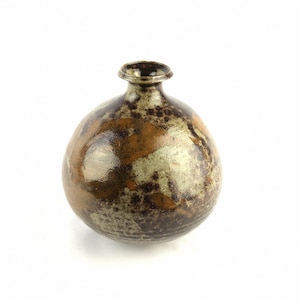May include: A round, brown ceramic vase with a mottled glaze. The vase has a wide base and a narrow neck.