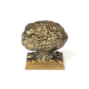 May include: A bronze-colored sculpture of a tree with a textured, rounded crown. The tree sits on a rectangular base with the words "MIDWEST FEDERAL" engraved on it. The sculpture is set against a white background.
