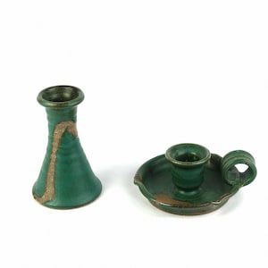 May include: Two green ceramic candle holders with a brown glaze. One is a tall, slender vase-shaped holder and the other is a smaller, round holder with a handle.
