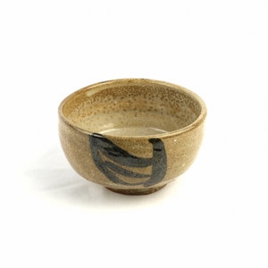 Op de afbeelding: Een kleine, bruine keramische kom met een zwart ontwerp. De kom heeft een gespikkeld glazuur en een afgeronde vorm.