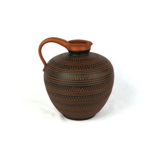 May include: A brown ceramic pitcher with a black and brown geometric pattern. The pitcher has a wide base and a narrow neck with a handle.