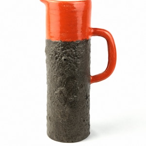 May include: A ceramic jug with a textured black body and a bright orange top. The jug has a handle and a spout.